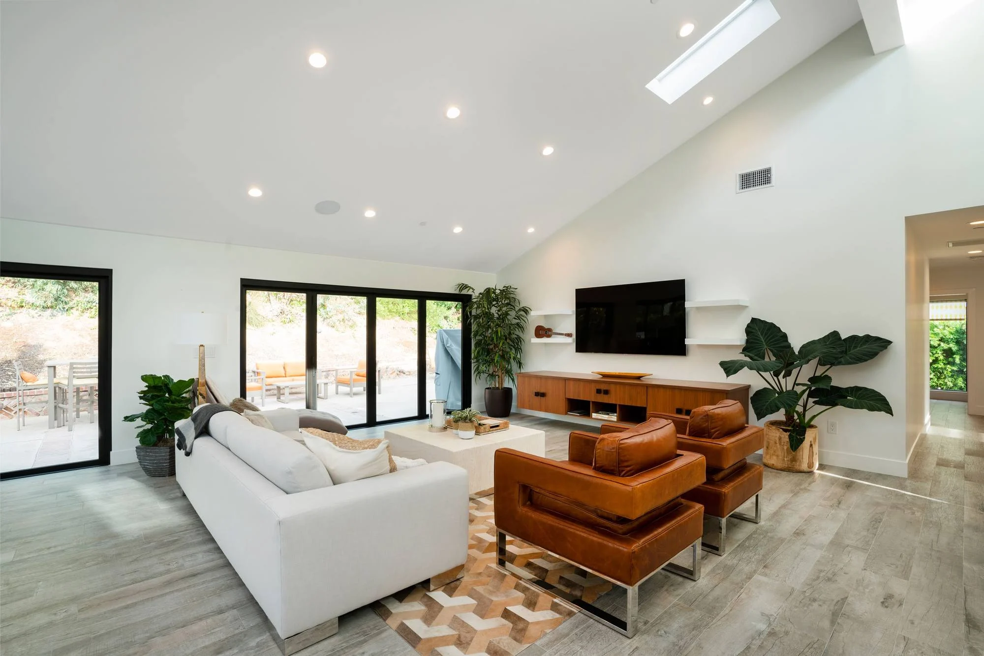 Vaulted living room with skylights, white sofa, cognac leather chairs and folding glass doors