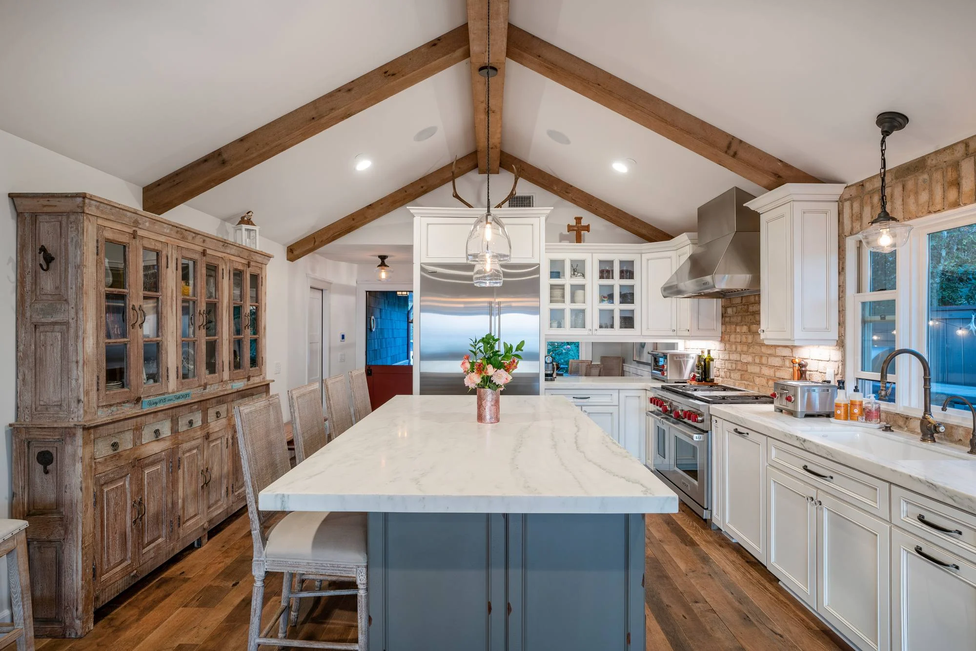 Vaulted kitchen with white cabinets, marble-topped gray island, brick backsplash and antique wood hutches