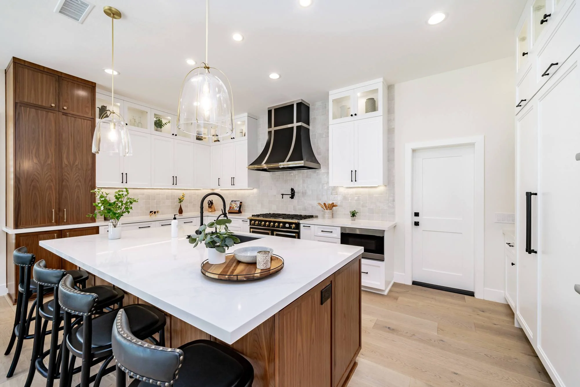 White kitchen with walnut island, black and brass range hood and glass pendants