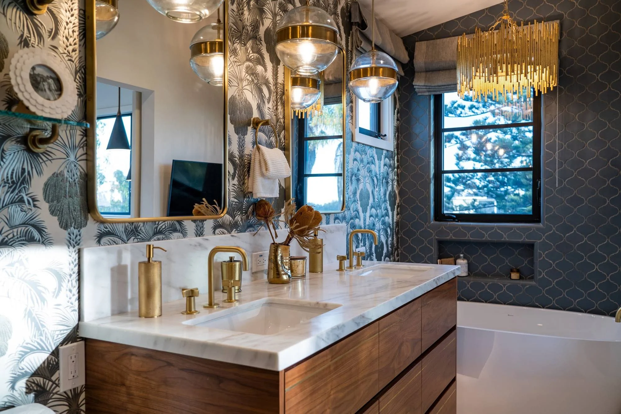 Primary bath with walnut double vanity, marble counter, brass fixtures and bold botanical wallpaper
