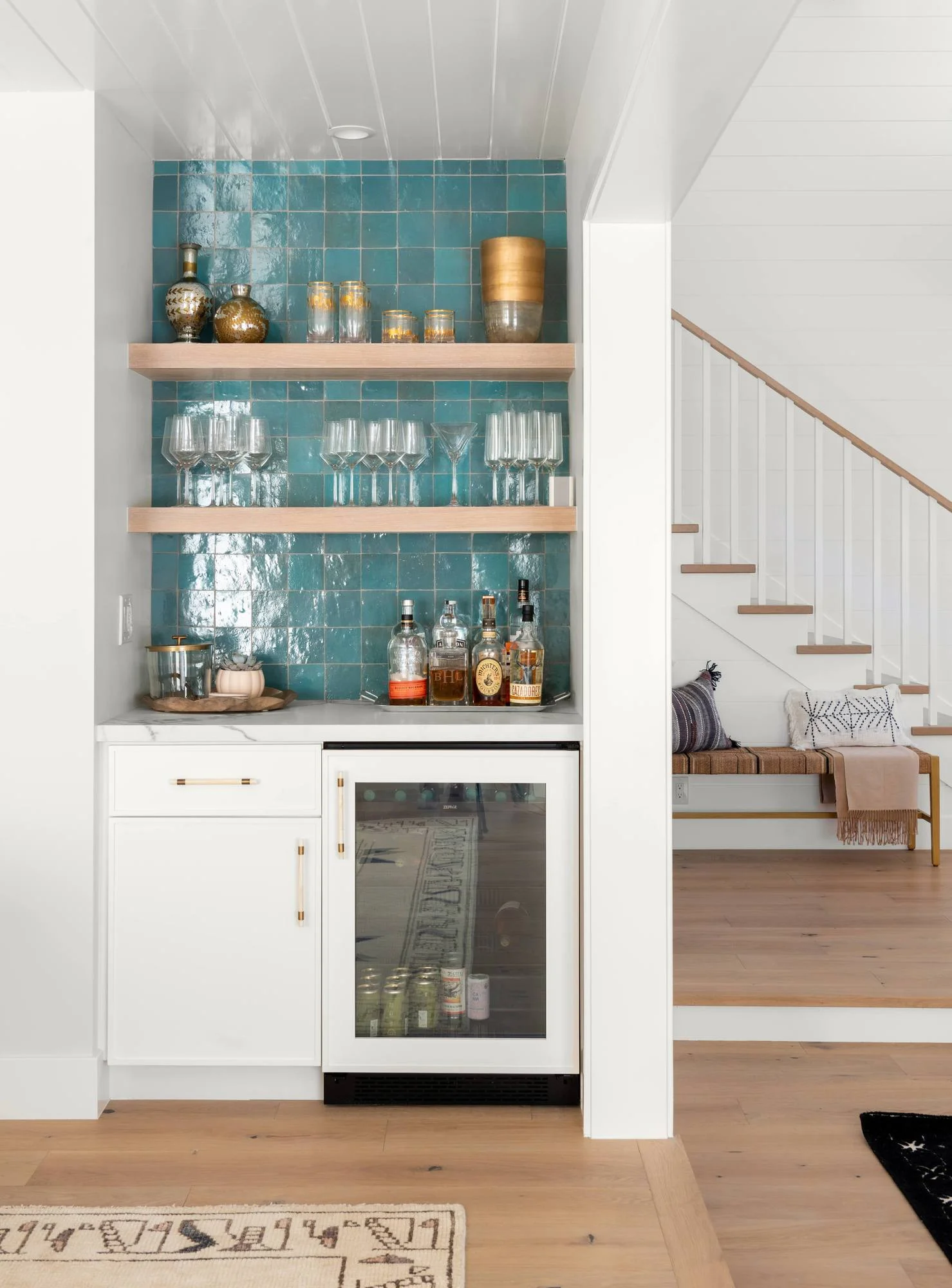 Wet bar with teal zellige tile, floating oak shelves and beverage fridge by the stair