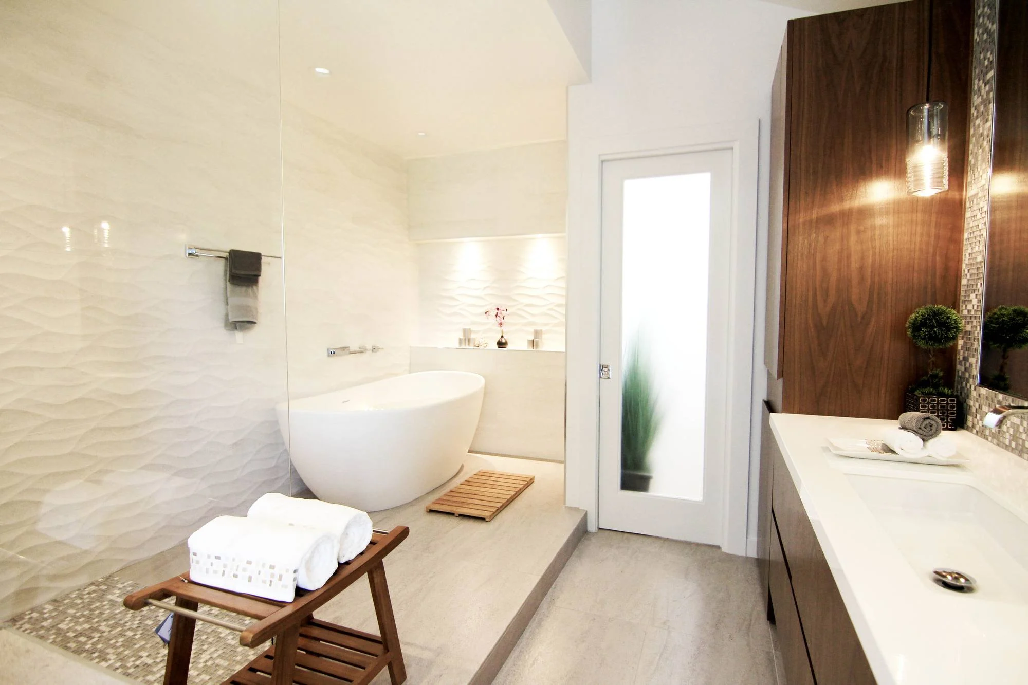 Spa-style primary bath with freestanding tub, wave-textured white tile and walnut vanity