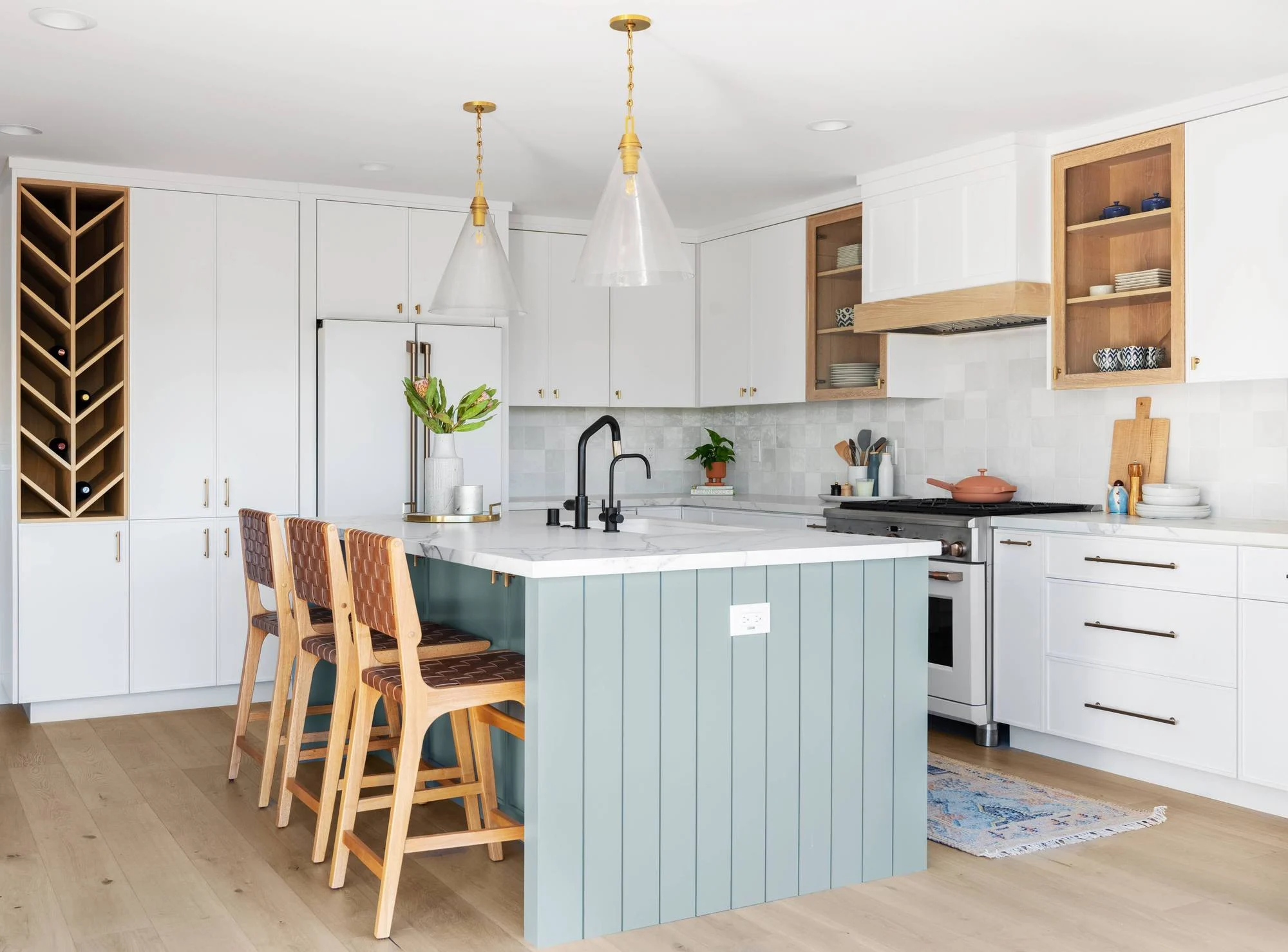 White kitchen with sage beadboard island, leather stools, brass pendants and wine cubby