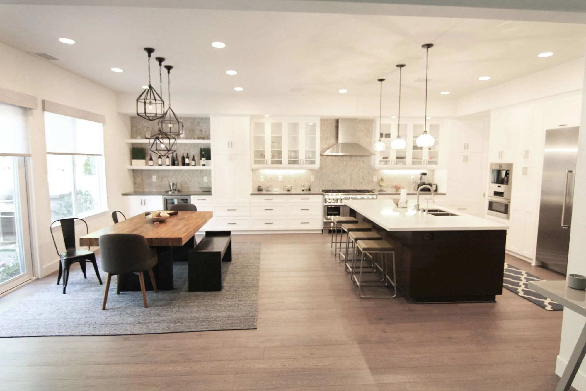 Open white kitchen with dark-stained island, pendant lights and a live-edge dining table on wide-plank floors