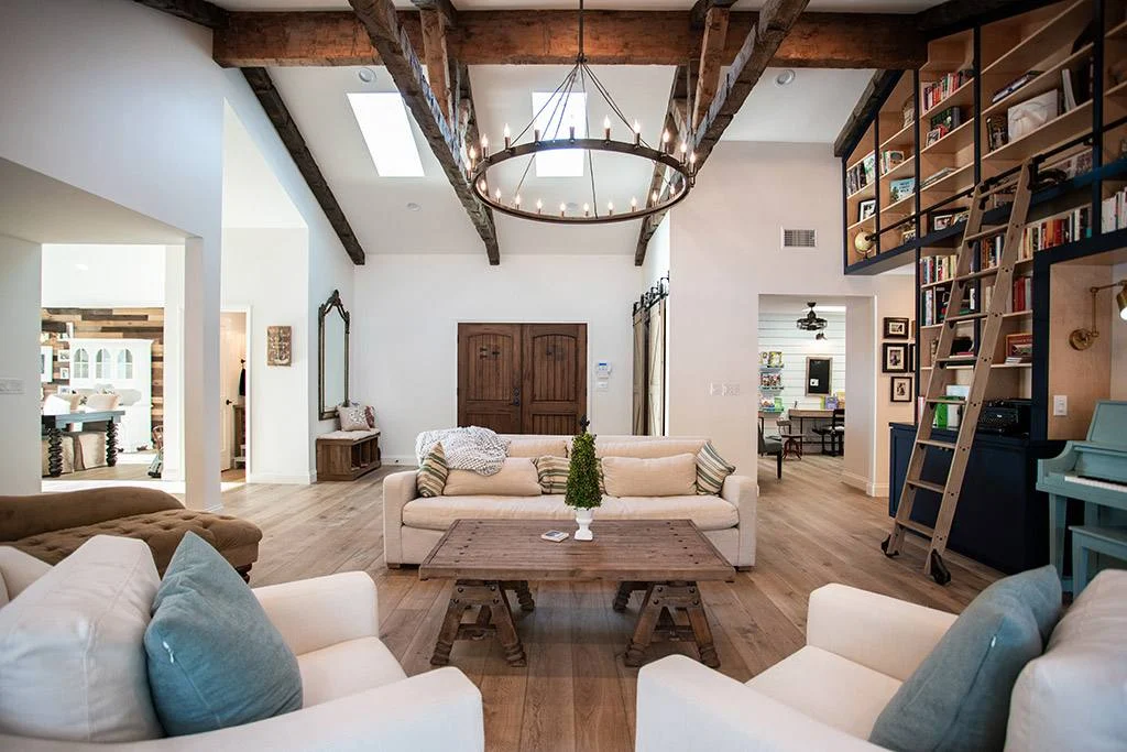 Vaulted great room with exposed wood beams, iron chandelier and a two-story library wall with rolling ladder