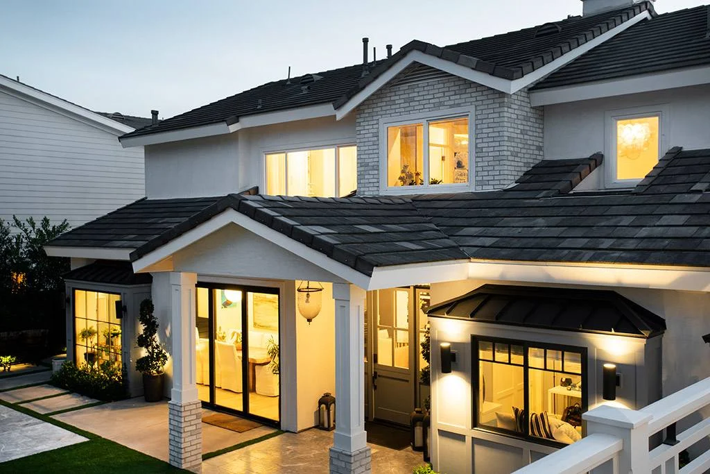 Rear of a two-story Cape Cod-style home at dusk with lit windows, covered porch and white railings