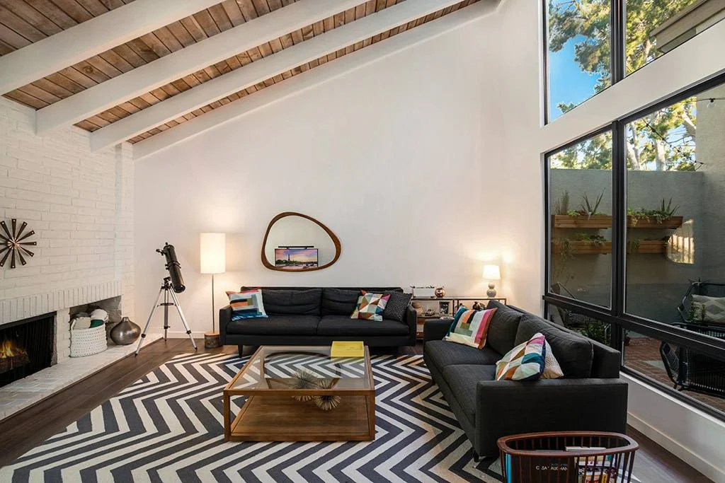 Living room with white-painted beams under a wood plank vaulted ceiling, white brick fireplace and chevron rug