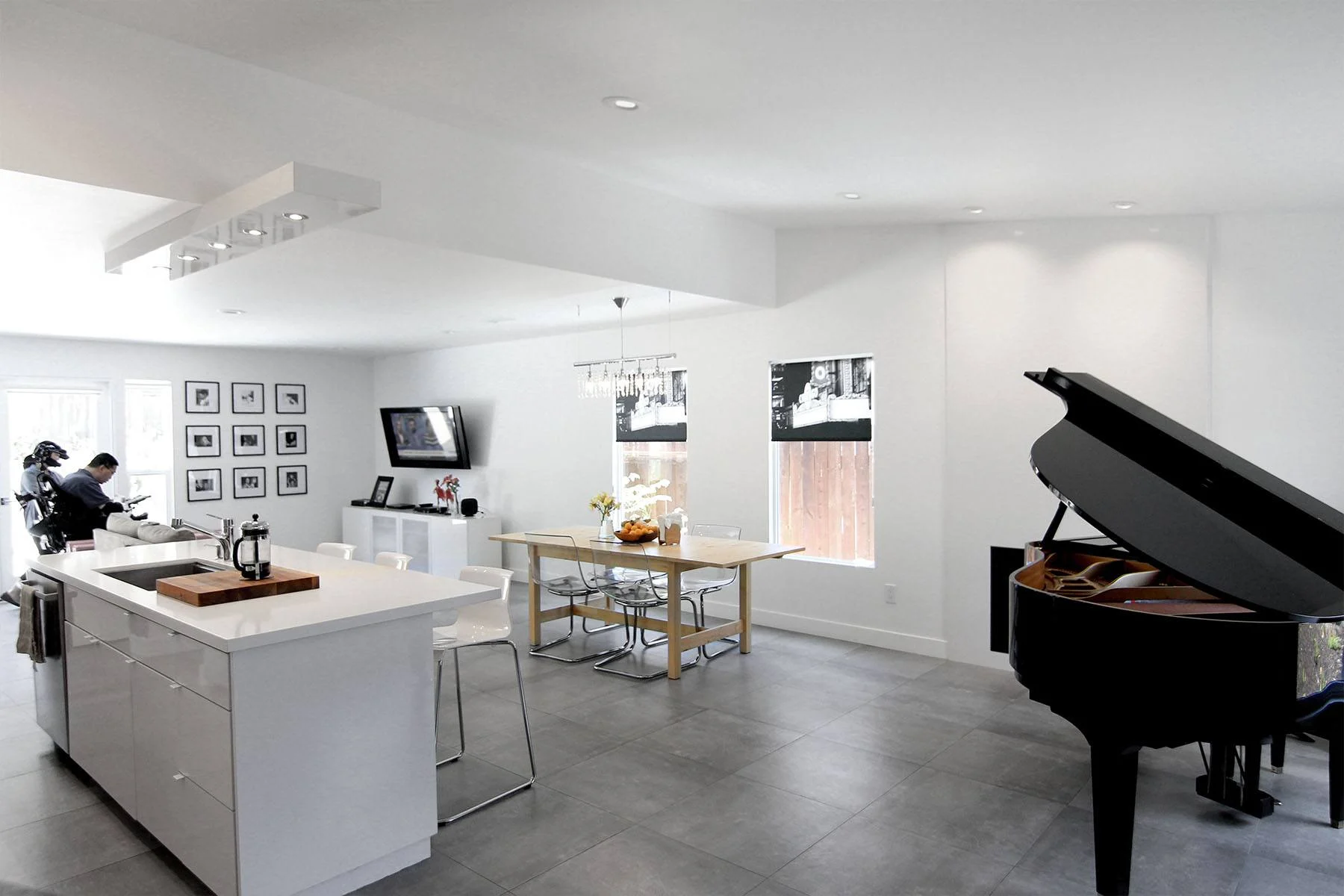 Open white great room with glossy kitchen island, polished concrete floors, gallery wall and grand piano