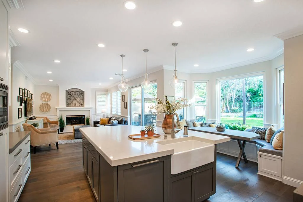 White kitchen with navy island, farmhouse sink, glass pendants and dark wood floors