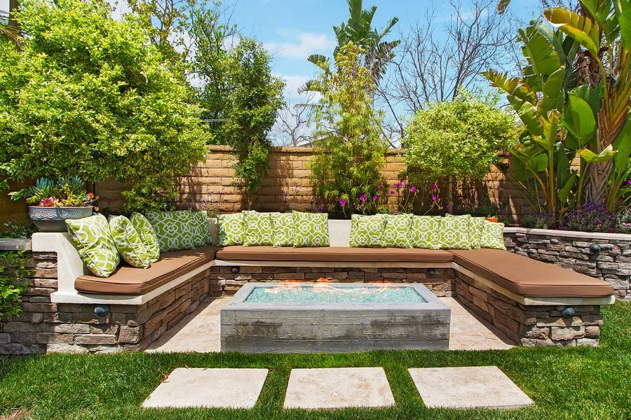 Backyard with stone-faced built-in bench seating around a fire pit, stepping pavers and lush planting
